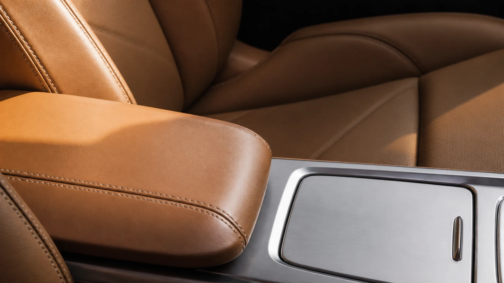 Close view of cognac leather seating, precise stitching and a brushed aluminium vehicle console.