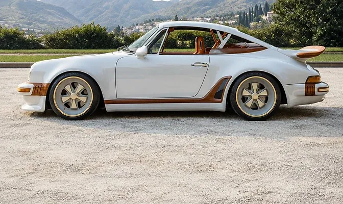 White sports coupe with copper accents below wooded mountains.